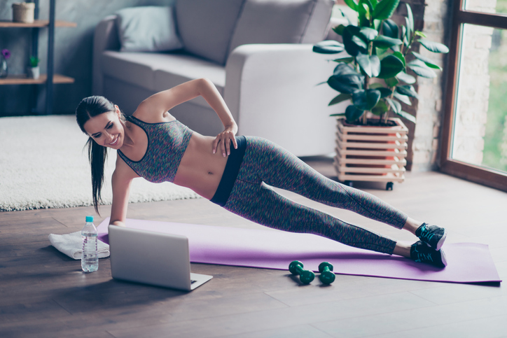 Beautiful sporty cheerful woman is doing side plank exercise She is watching video on the internet and repeating the tasks Startlap Vásárlás