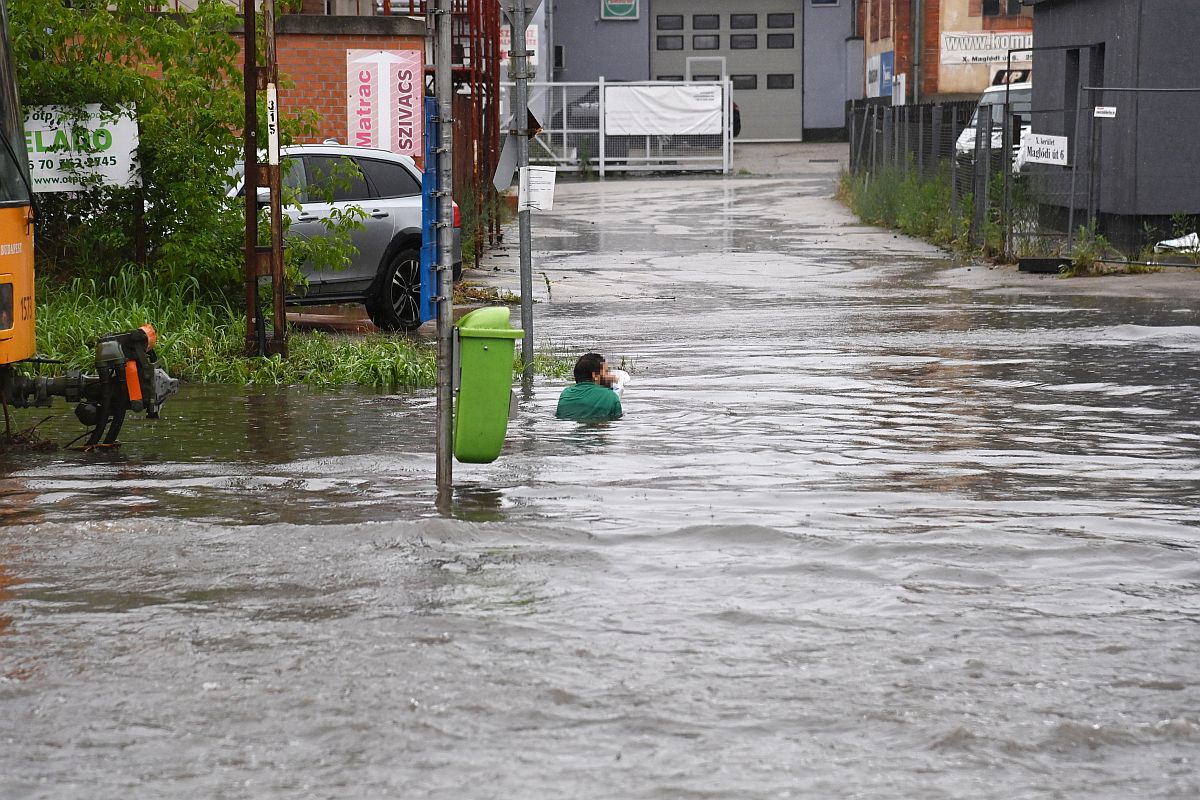 A felgyülemlett esővízben ül egy féri, akinek a lába a villamossínek közé szorult a Maglódi úton 2023. június 9-én.