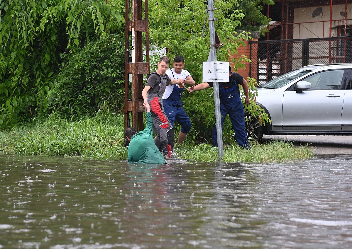 Egy férfit segítenek ki a felgyülemlett esővízből, akinek a lába a villamossínek közé szorult a Maglódi úton 2023. június 9-én.