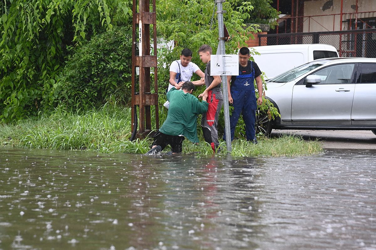 Egy férfit segítenek ki a felgyülemlett esővízből, akinek a lába a villamossínek közé szorult a Maglódi úton 2023. június 9-én.
