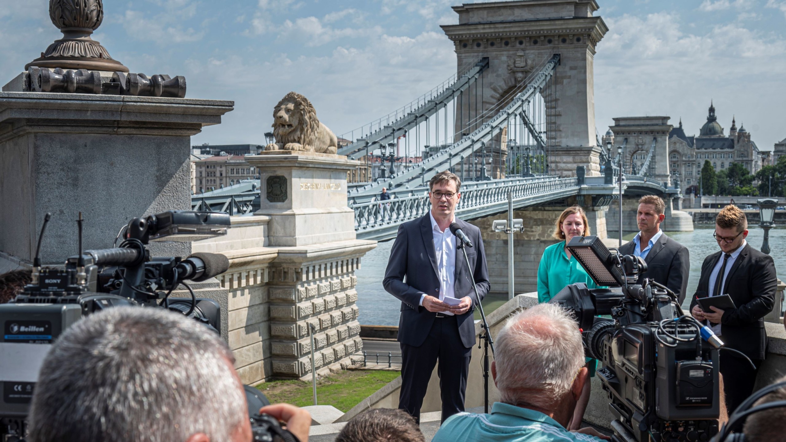 Karácsony Gergely főpolgármester beszédet mond a felújított Lánchíd átadásán a híd budai hídfőjénél 2023. augusztus 4-én. Mögötte Walter Katalin, a Budapesti Közlekedési Központ (BKK) vezérigazgatója (b2) és Csohány András, a kivitelező A-Híd Zrt. vezérigazgatója (b3).