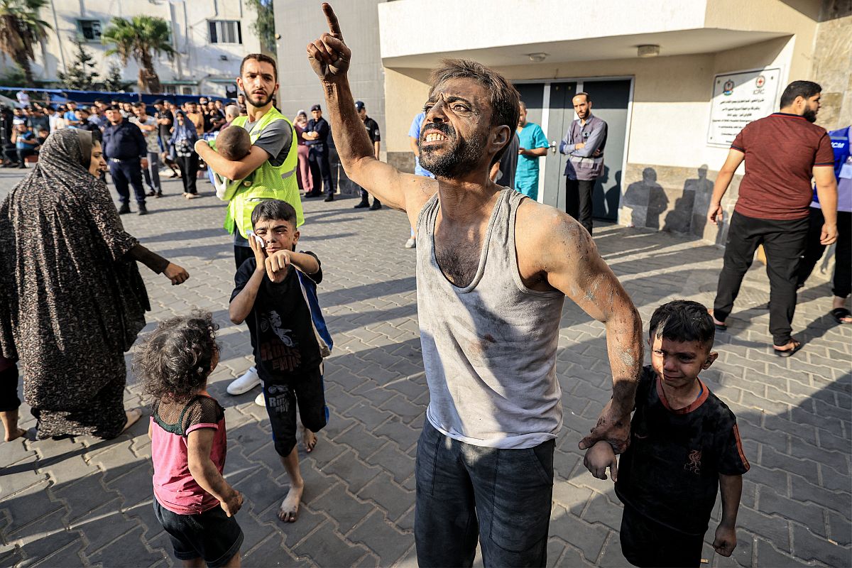 Egy palesztin férfi egy gyerek kezét fogja egy gázavárosi kórház épülete előtt.