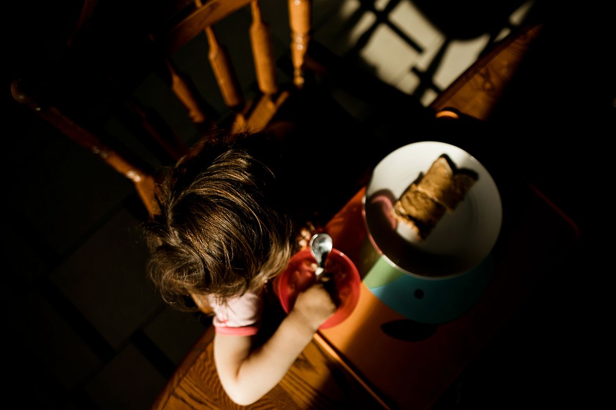 Egy fentről fotózott gyerek ül egy asztalnál, előtte tányér, kezében kanál.