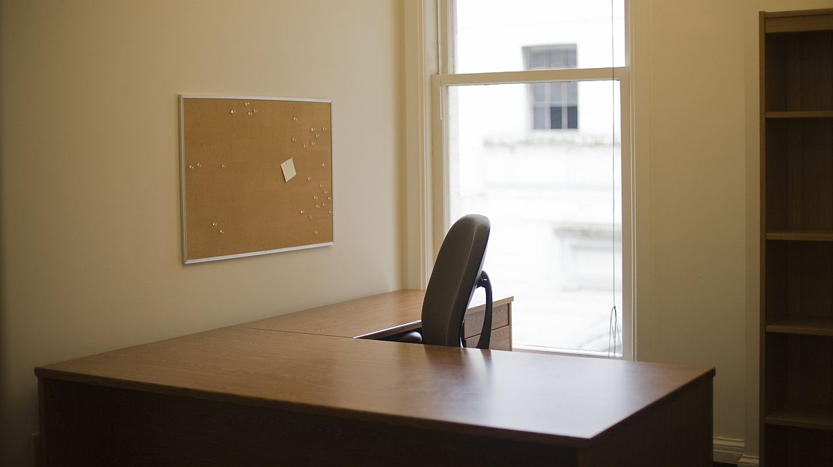 Egy iroda üres irodai asztallal, irodaszékkel, szekrénnyel.
