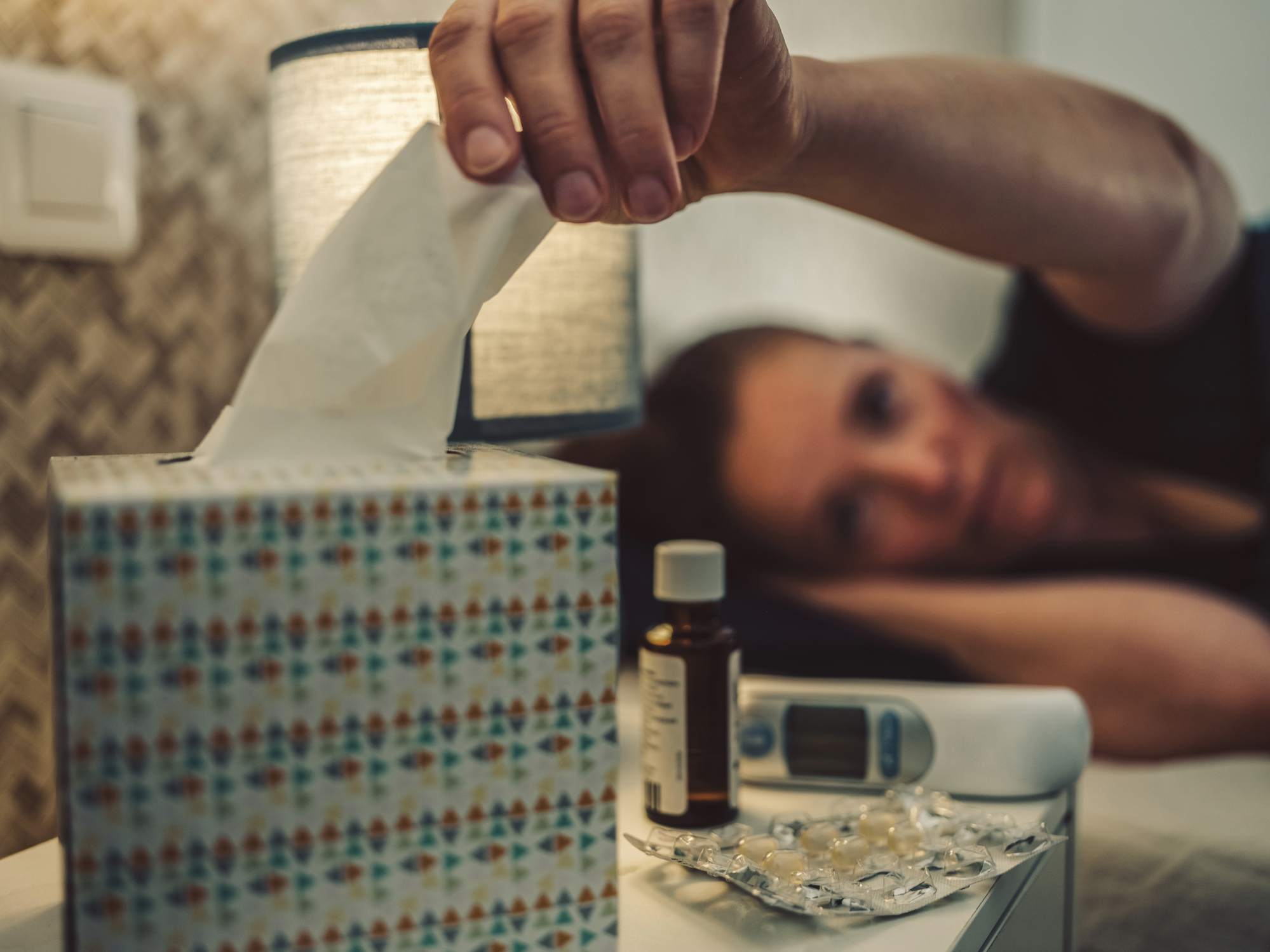 Zsepkendőért nyúló ágyban fekvő nő