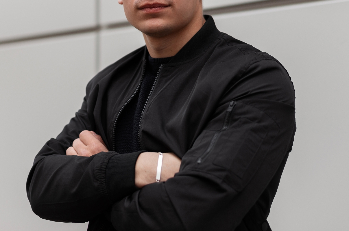 Fiatal férfi fekete dzsekiben, karját mellkasa előtt átkulcsolva áll úgy, hogy az arca nem látszik a fényképen