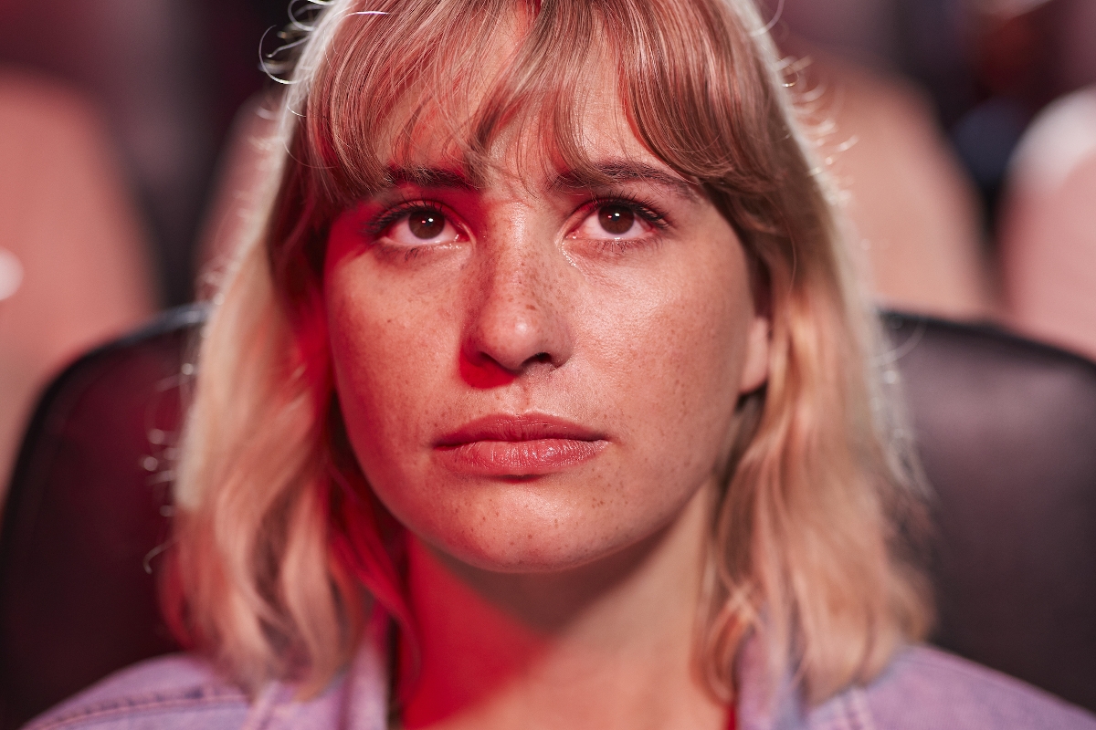 Egy fiatal nő arca közelről, ahogyan komoran néz egy moziban