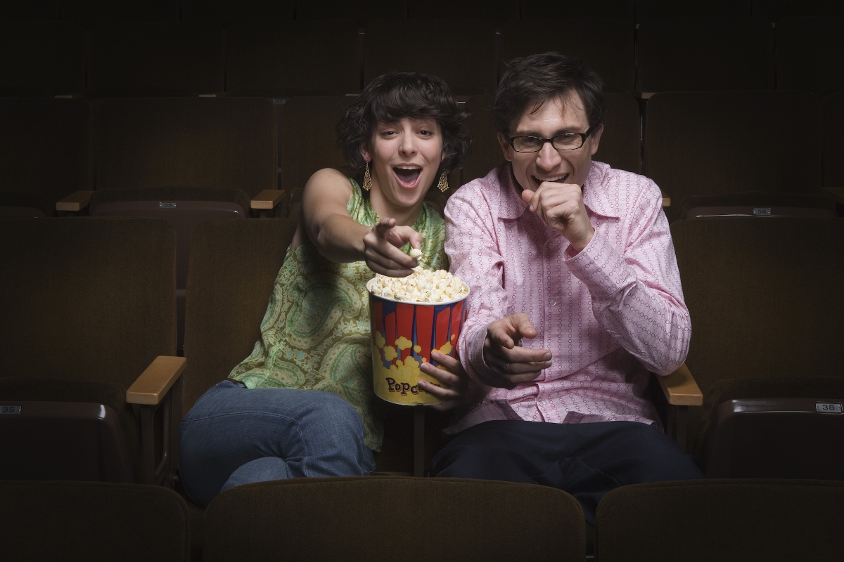 Egy moziban ülő nő mutat a vászon felé, a kezében egy vödör pattogatott kukorica, mellette egy férdi, aki nevet