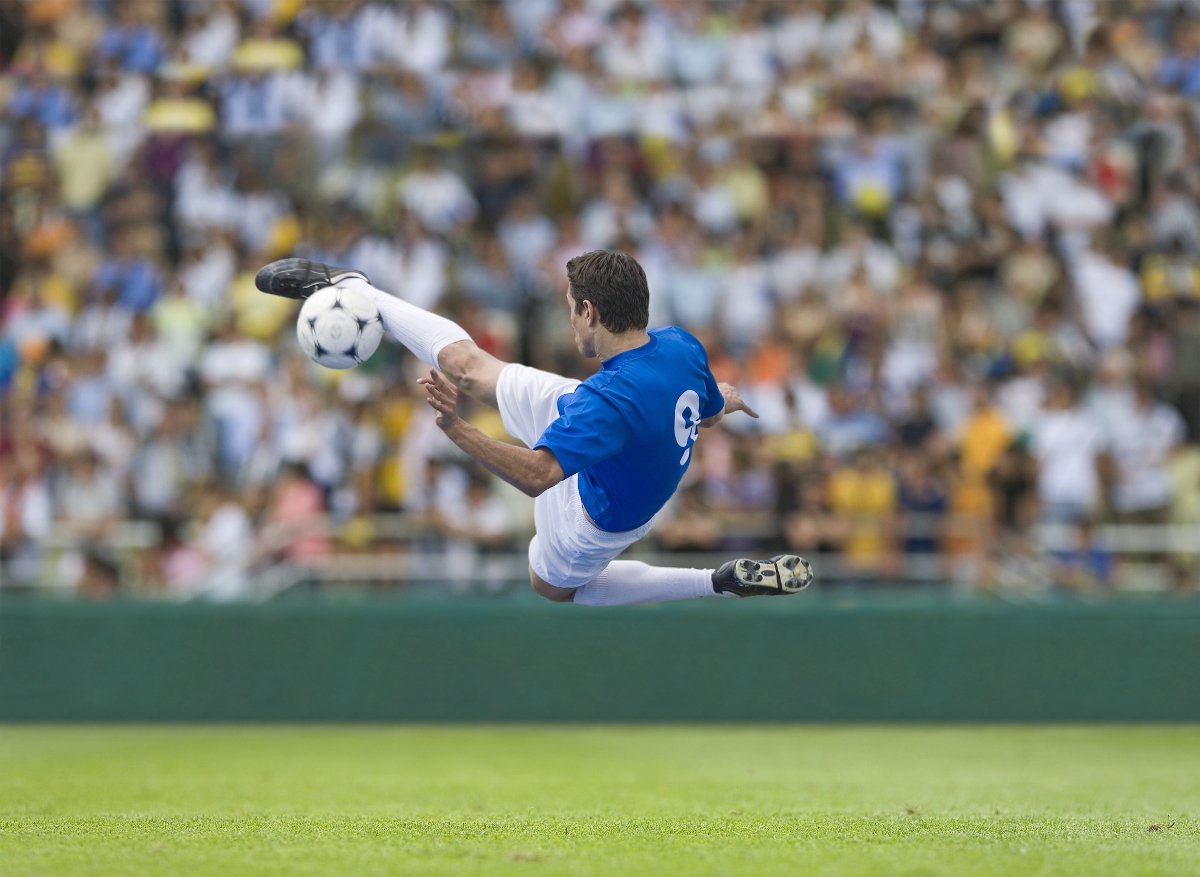 Egy focista a levegőbe emelkedik, miközben megrúgja a labdát
