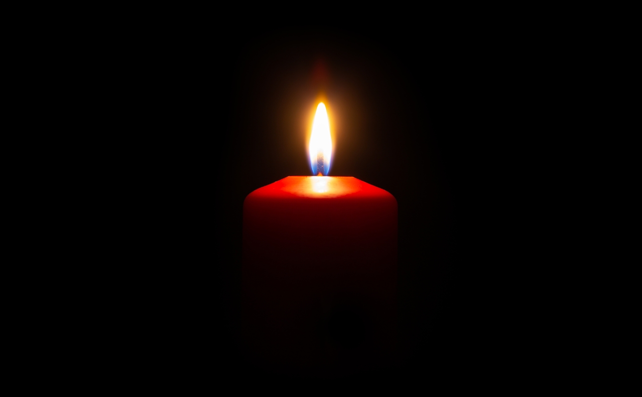 Egy vörös gyertya ég sárga lánggal a sötét háttér előtt