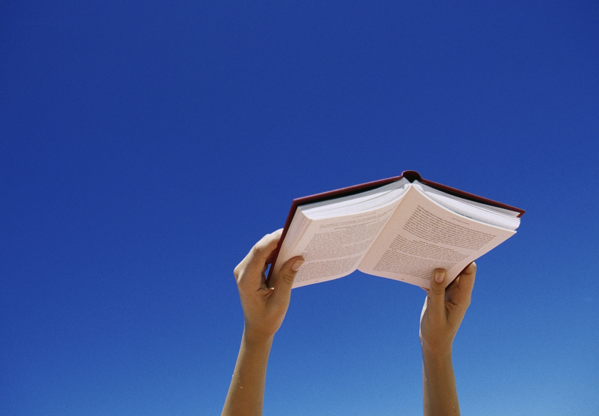 Könyv a kézben, a háttérben az égbolt kékje látható