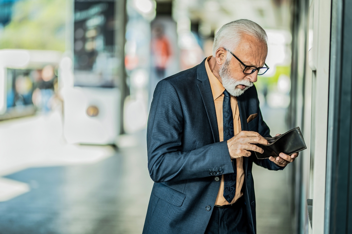Egy kék színű zakót viselő férfi vizslatja a pénztárcáját