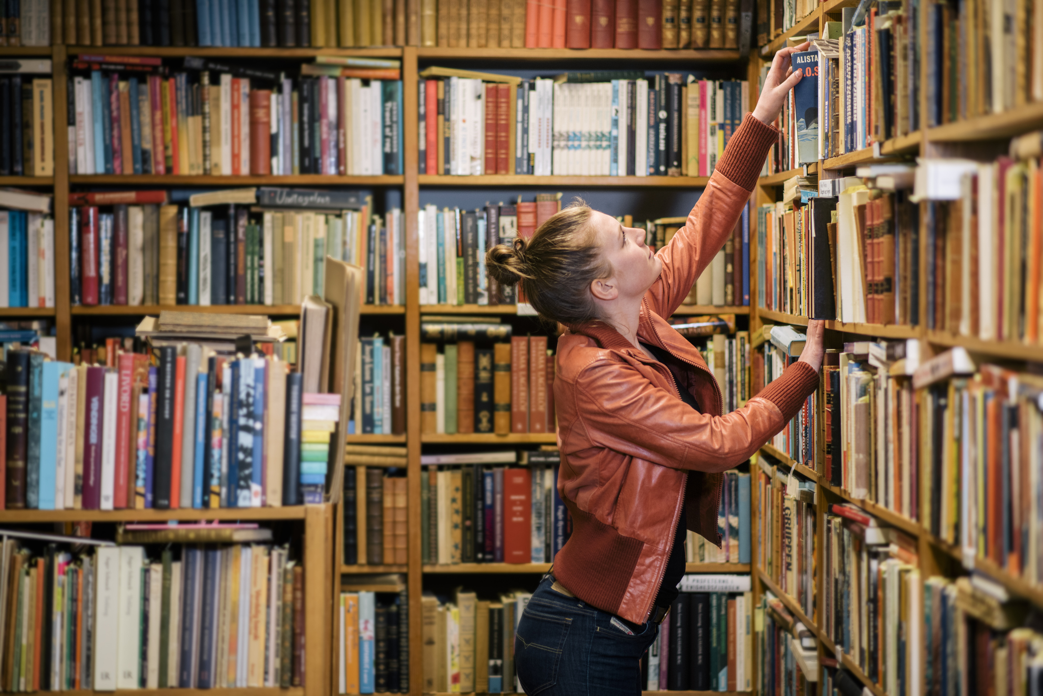 Egy fiatal nő felnyúl a polcra egy könyvesboltban