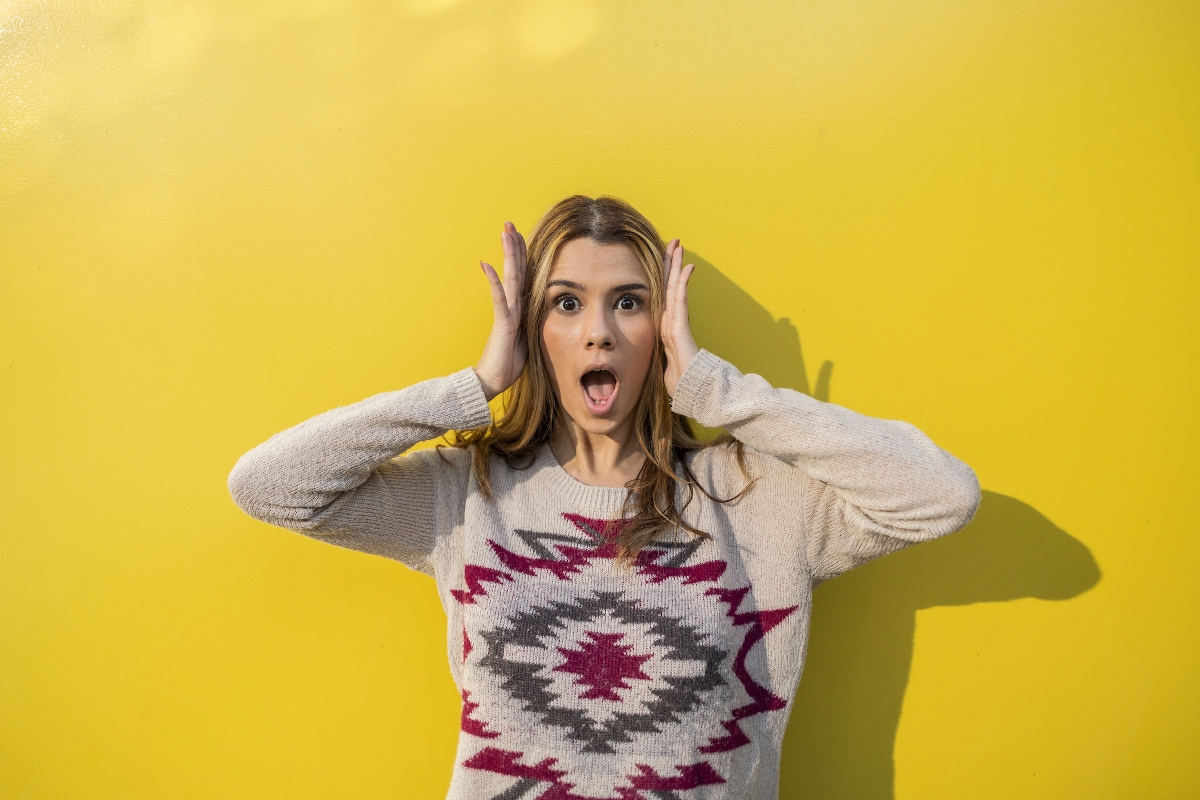 Fiatal nő csodálkozásra tátja a száját egy mintás pulóverben