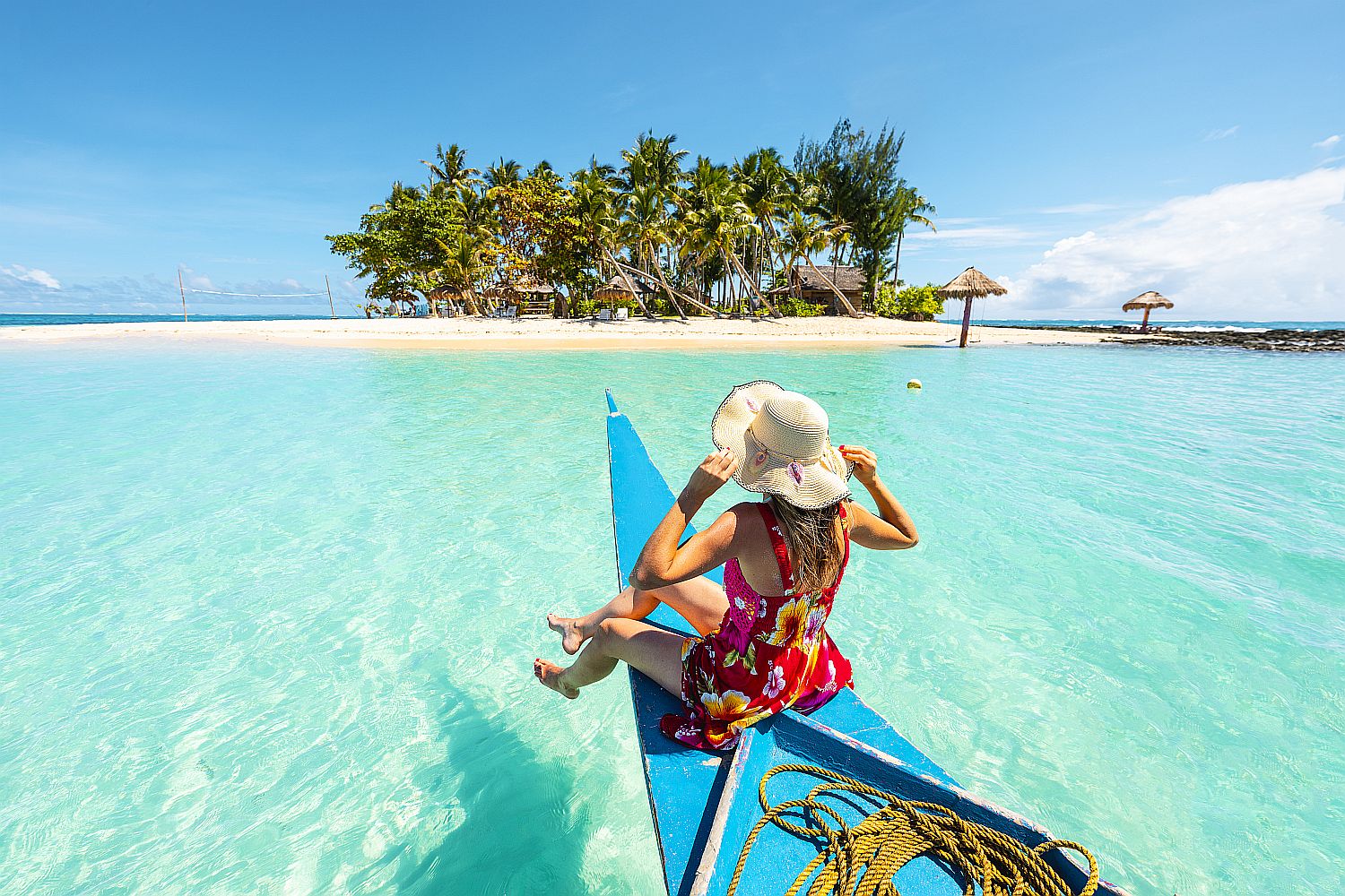 Woman sitting on bangka boat approaching a tropical island - Startlap Egy szalmakalapos nő egy csónak orráról a tengerbe lógatja a lábát egy pálmafás sziget közelében