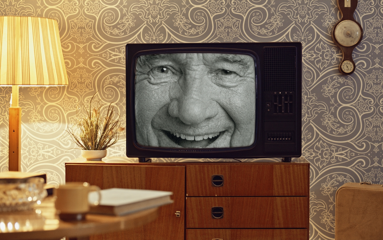 Egy mosolygó arc jelenik meg egy fekete-fehér katódsugárcsöves televízión