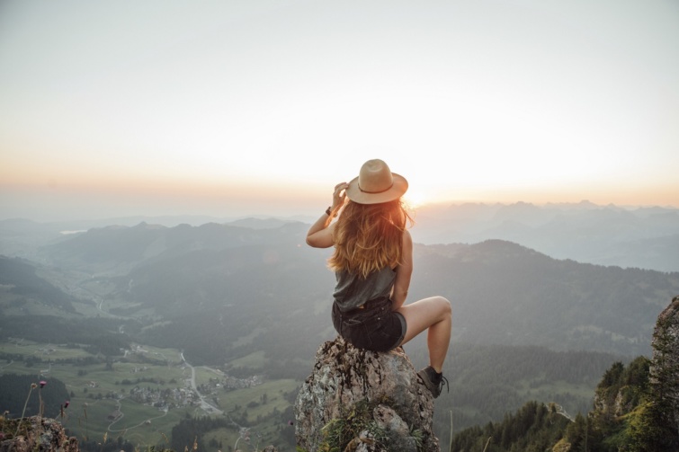 Nő ül egy hegy tetején és nézi a tájat