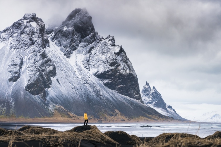 Ember áll a magas hegyek előtt Izlandon.