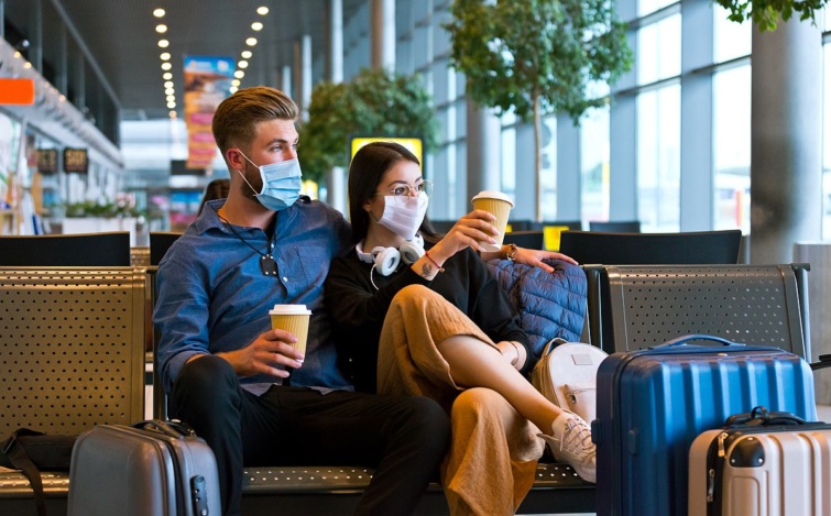 Egy fiatal pár maszkban várakozik a repülőtéren