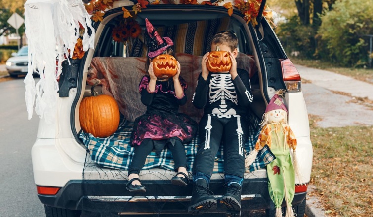 Halloween-jelmezes gyerekek ülnek egy utcán parkoló autó csomagterében.
