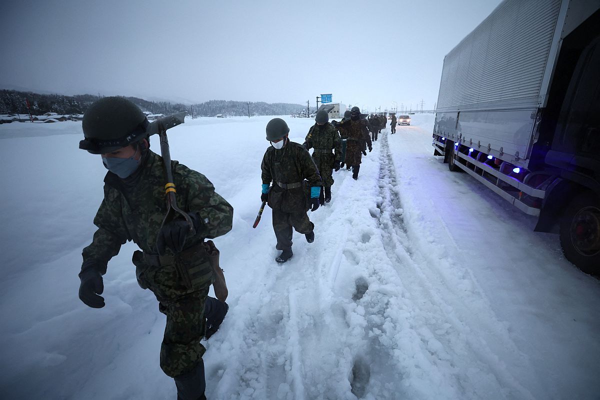 A japán Önkéntes Védelmi Erők emberei menetelnek a hóban az elakadt járművek mellett Niigata tartományban 2022.12.20-án.