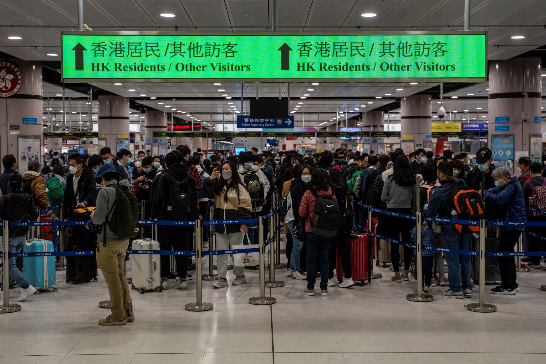 Arcmaszkot viselő utazók sorban állnak a határátlépésre a Lok Ma Chau határátkelőnél 2023. január 8-án Hongkongban.