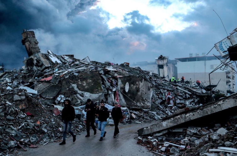 Összedőlt lakóház romjai előtt gyalogolnak emberek a dél-törökországi Hatay tartományban lévő Iskenderunban 2023. február 7-én a nagy török-szíriai földrengés után