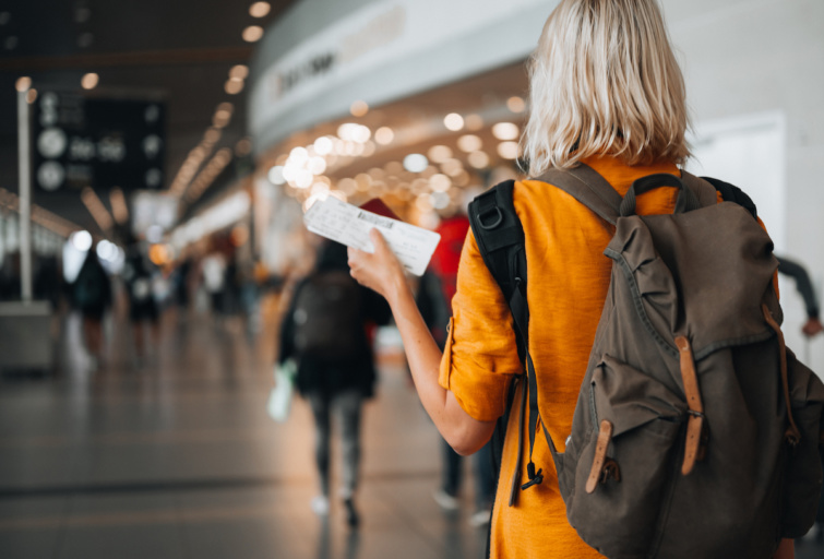 Egy nő megy a reptéren a járatához, kezében a repülőjegyekkel