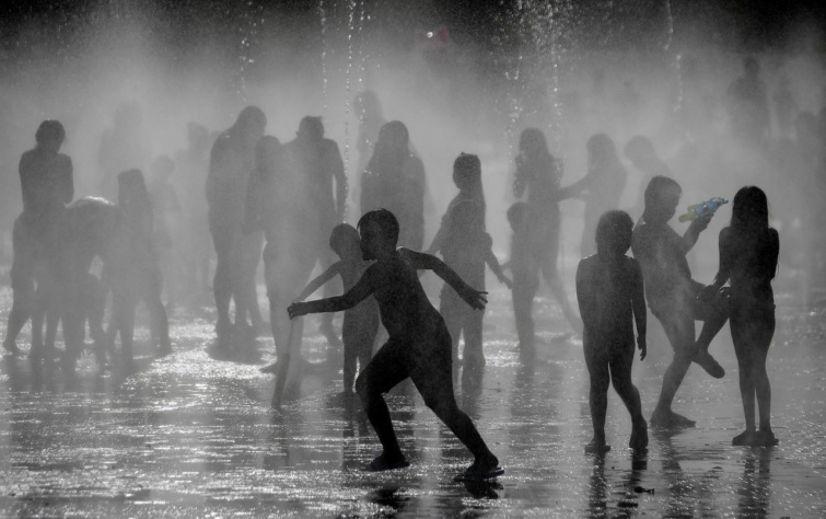 Emberek szökőkutak alatt állnak a Manzanares folyó mellett, hogy lehűljenek a forró időben Madridban.