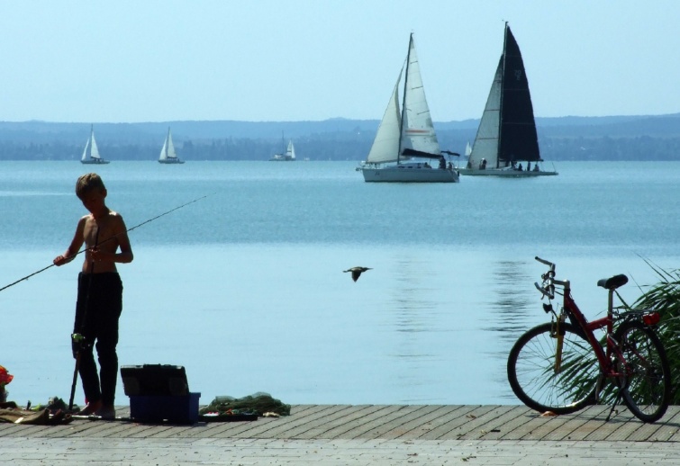 Egy kerékpárral érkezett horgász fiú a Balaton-parton elõkészíti halfogó eszközeit.