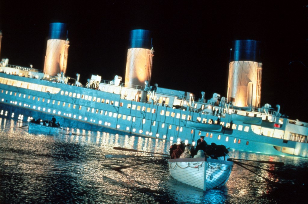 A Titanic filmjelente, háttérben a süllyedő hajóval, előtérben egy mentőcsónakkal