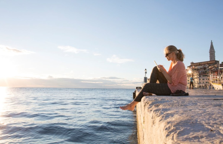 Egy nő ül Horvátországban a tengerparton, kezében egy telefonnal