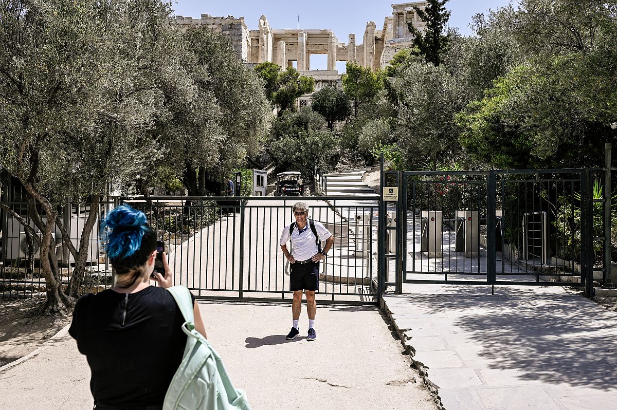 Egy férfit fotóz egy nő az athéni Akropolisz bezárt kapuja előtt.