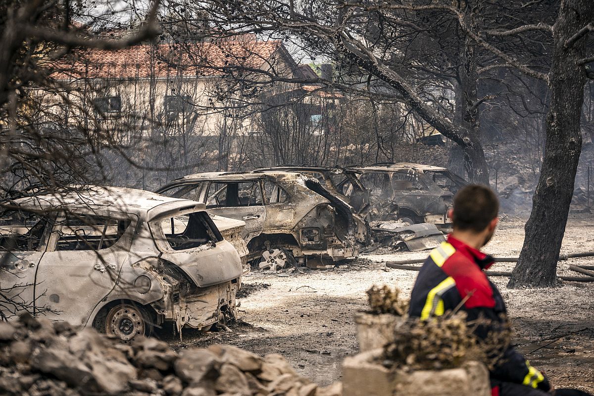 Erdőtűzben kiégett autók roncsait nézi egy tűzoltó.
