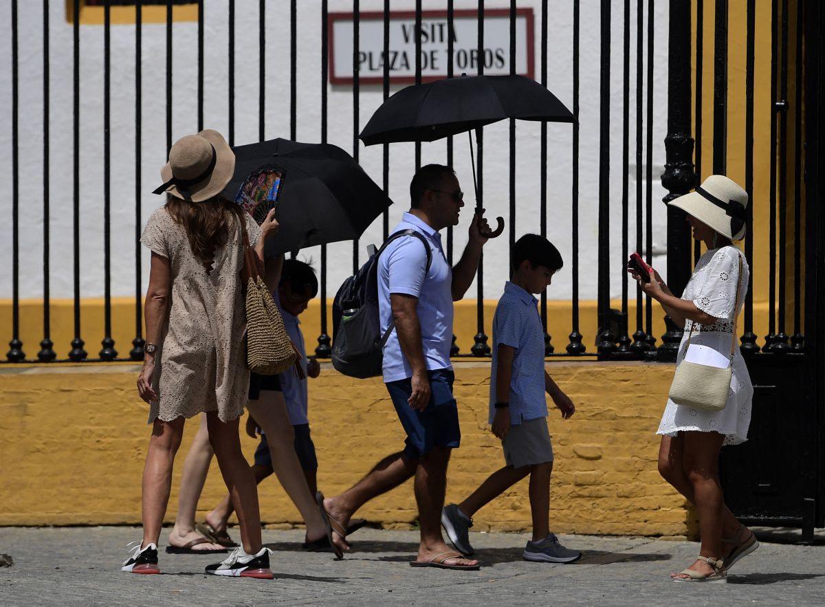 Fejük fölött esernyőt tartó emberek az utcán a hőségben.