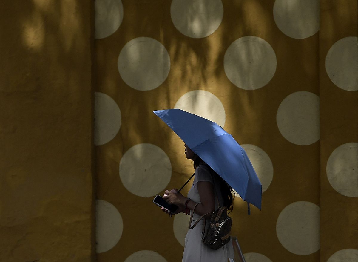 Egy esernyőt tartó nő megy el egy pöttyös mintájú fal előtt.