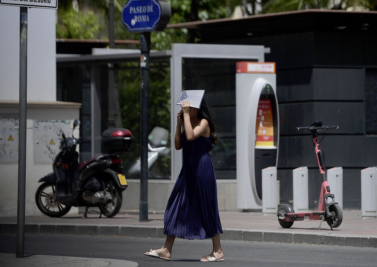 Egy nő egy mappát tart a feje fölött a hőségben az utcán.