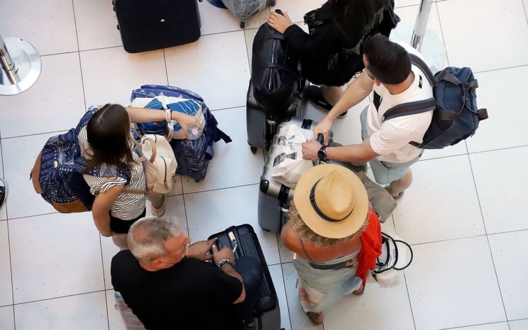 Sorban álló utasok a bőröndjeikkel egy reptéren.