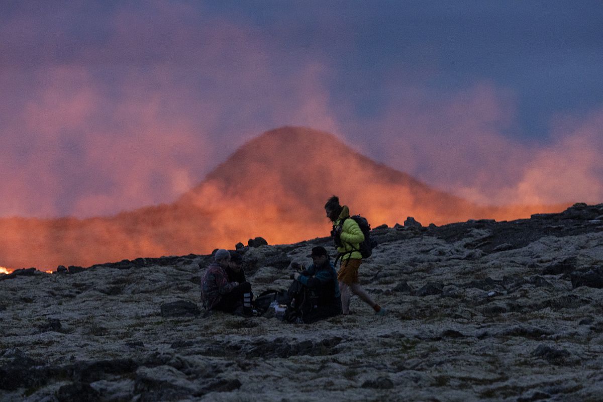 Három ember néz egy fortyogó vulkánt.