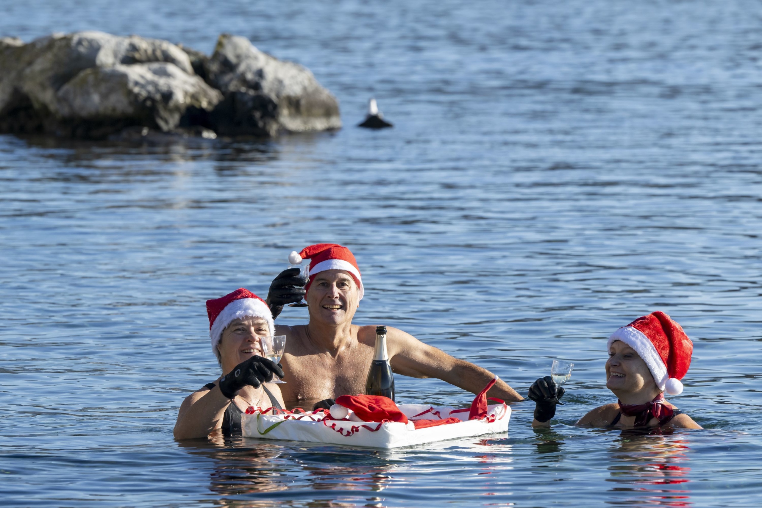 Mikulássapkát viselő emberek pezsgőt isznak a Genfi-tó 8 Celsius-fokos vizében rendezett hagyományos karácsonyi úszáson Genfben.