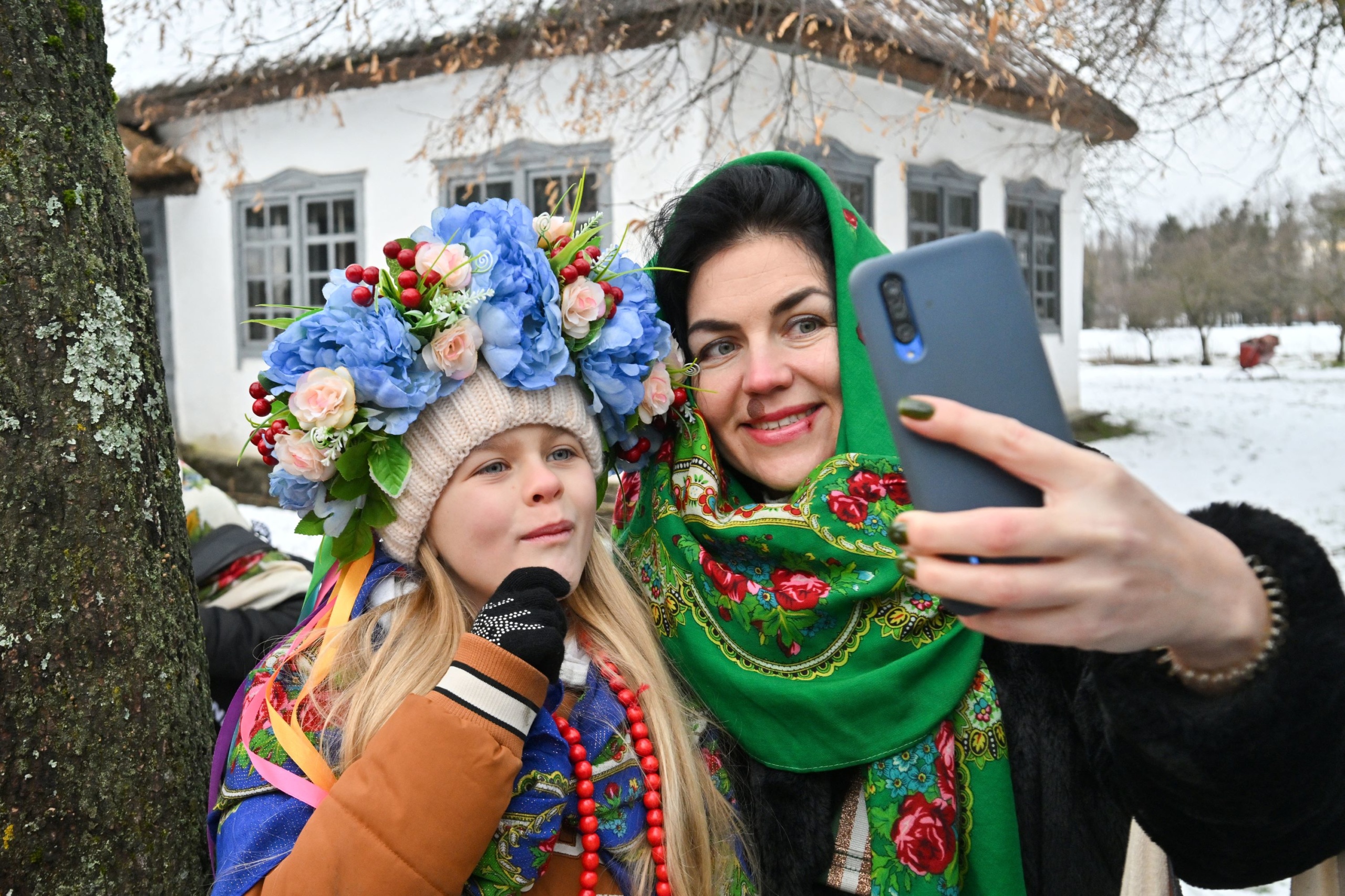 Egy hagyományos ukrán ruhát viselő nő és egy fiatal lány szelfit készít, miközben karácsonyi ünnepségen vesznek részt a Kijev melletti Pirogov faluban