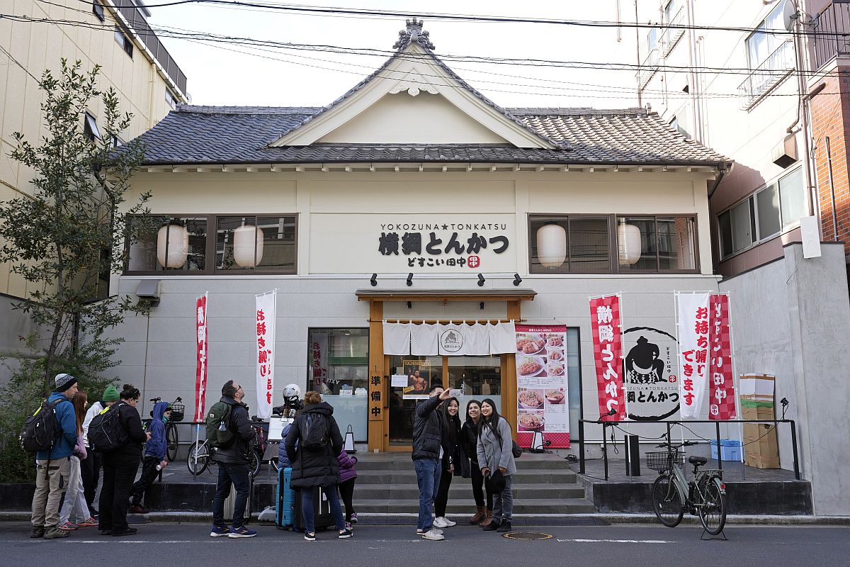 Külföldi turisták állnak sorban egy szumóbemutató előtt a tokiói Jokozuna Tonkacu étteremnél.