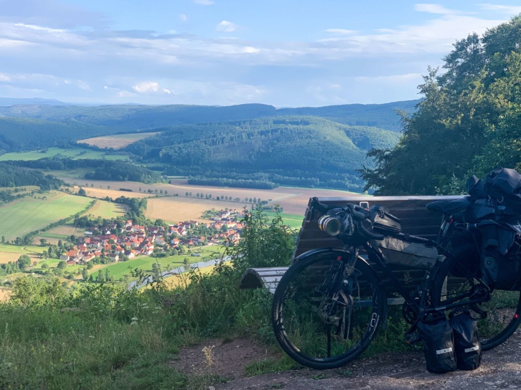 Gyönyörű látkép egy domboldalról egy kisvárosra, egy pad mellett a dombon Ricsi megpakolt biciklije látható