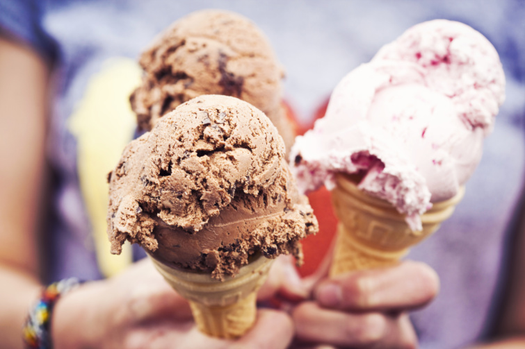 Két csokoládé és egy rózsaszín színű fagylaltot tart három emberi kéz