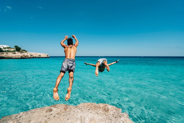 Gyönyörű kék víz egy spanyol szabadstrandon, a szikláról gyerekek ugrálnak a tengerbe