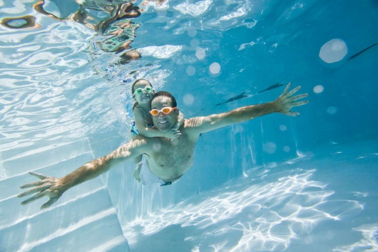 Úszó férfi és kisgyerek medencében víz alatt