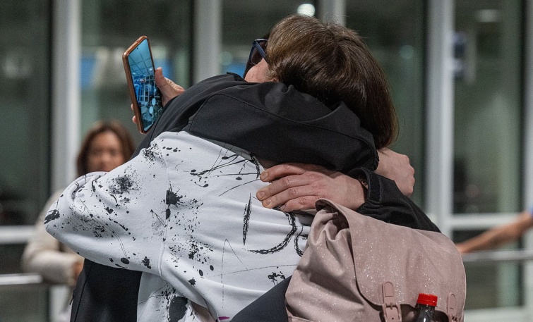 Egy hátizsákos, mobiltelefont a kezében tartó nőt ölel egy férfi.