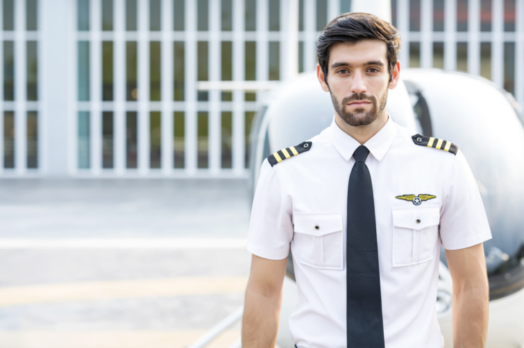 Fiatal barna haj férfi pilóta repülő előtt áll egyenruhában