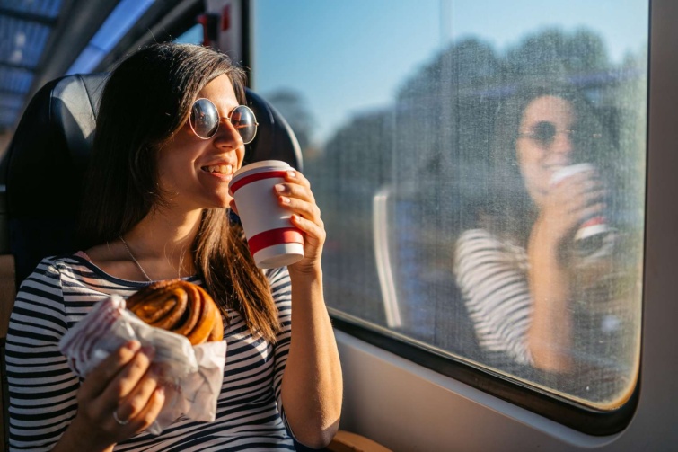 Napszemüveges lány kakaóscsigát eszik és kávét iszik a vonaton vidáman