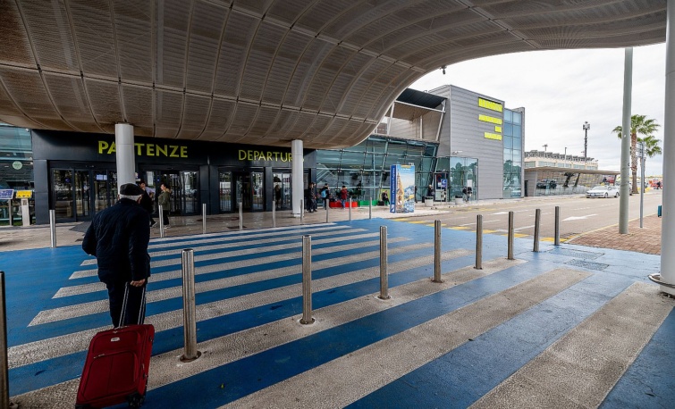 Egy idős utas bőröndöt húz egy repülőtér épülete előtt.